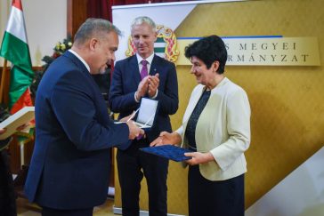 Csasztvanné Vass Edit átveszi a díjat Zalai Mihálytól, a megyei közgyűlés elnökétől. A háttérben Soltész Miklós, a Miniszterelnökség egyházi és nemzetiségi kapcsolatokért felelős államtitkára.