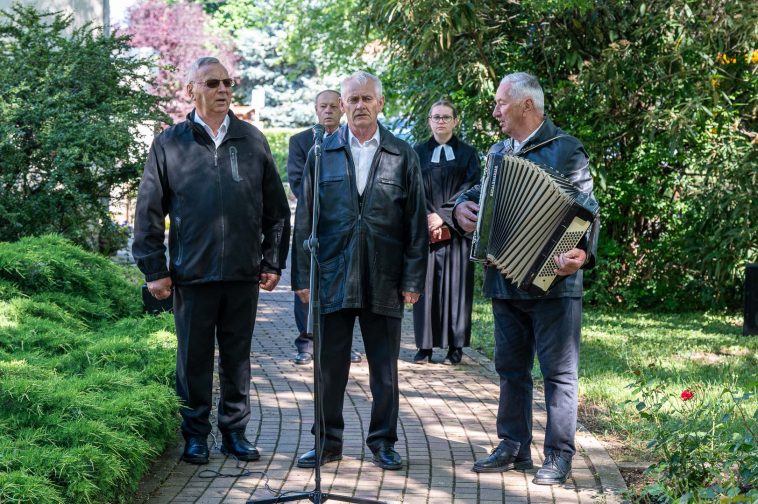 A Csabacsűdi Hagyományőrző Népdalkör és Citera Zenekar tagjai, Lipták András, Simon György és Major József katonadalokat adtak elő. A háttérben Molnár József polgármester és Magyar-Paulik Enikő evangélikus lelkész áll.